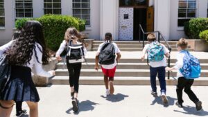 Students running into a school building, promoting a safe and welcoming environment as part of a campaign on how to stop bullying at school.