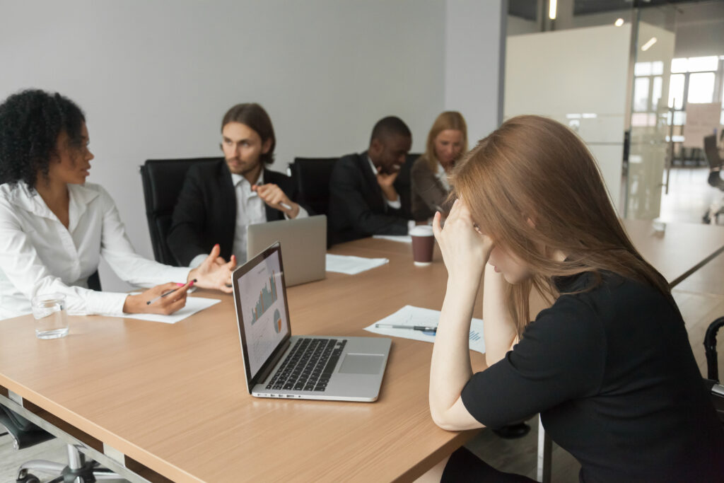 A distressed woman in a workplace meeting feeling isolated, highlighting the need for employment discrimination lawyers